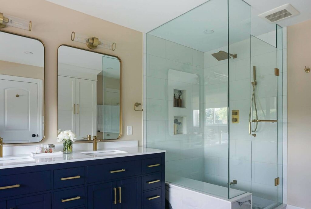 Side-view of glass door walk-in shower with gold finishes and blue cabinet vanity